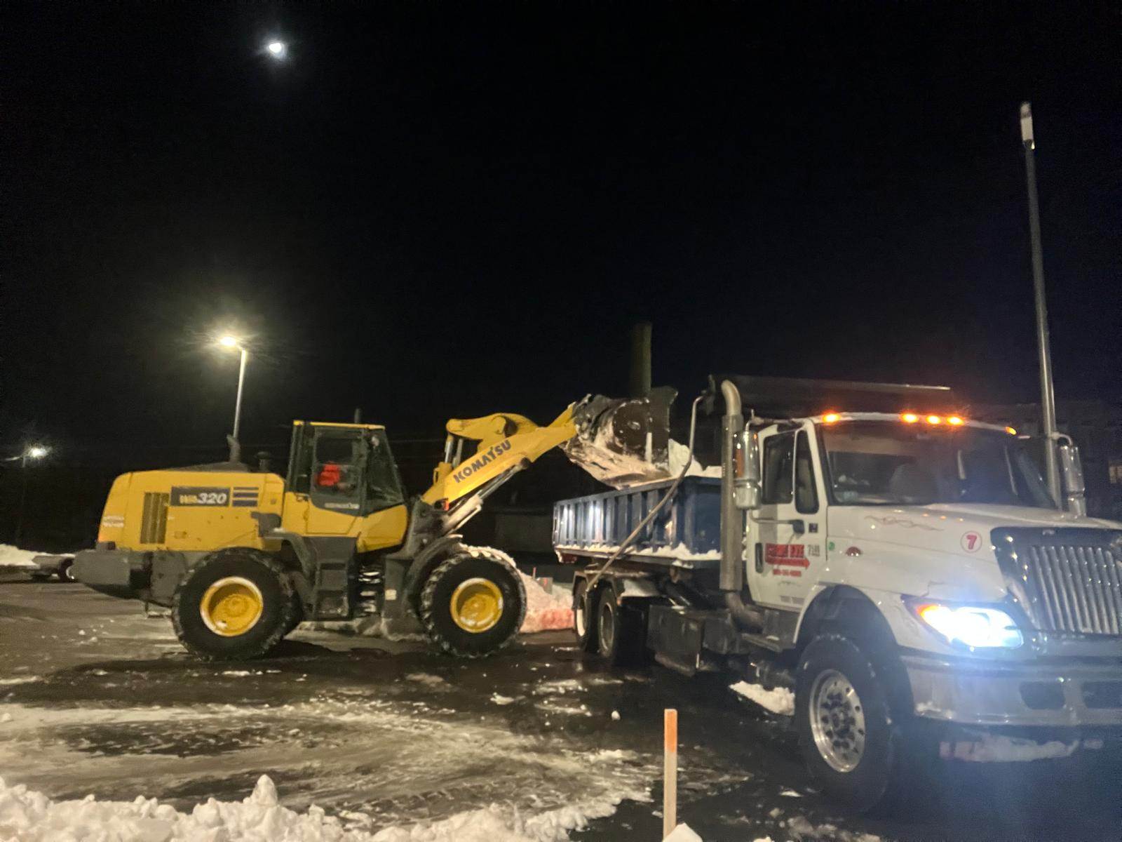 Tractor loading snow into a roll-off dumpster for winter property management